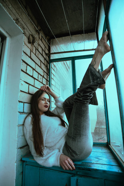 Beautiful young sexy girl posing on the balcony. Art photo portrait of a girl in a modern style with a sitting and added noise on the photo. - Photo, Image