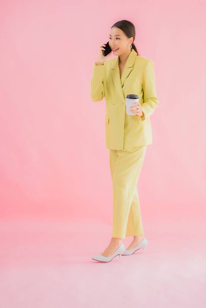 Portrét krásná mladá asijská obchodní žena používat chytrý mobilní telefon s šálkem kávy na barevném pozadí - Fotografie, Obrázek