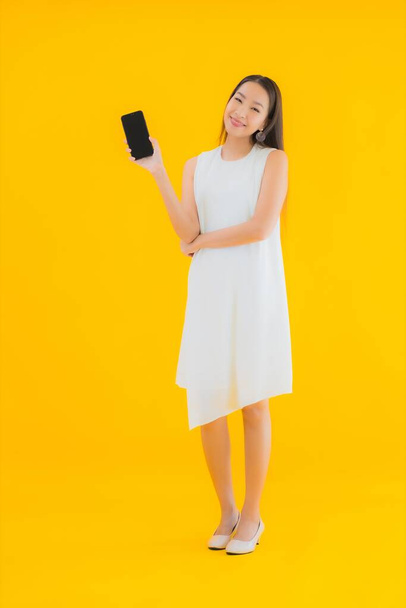 Portrait belle jeune femme asiatique avec téléphone portable intelligent sur fond jaune isolé - Photo, image