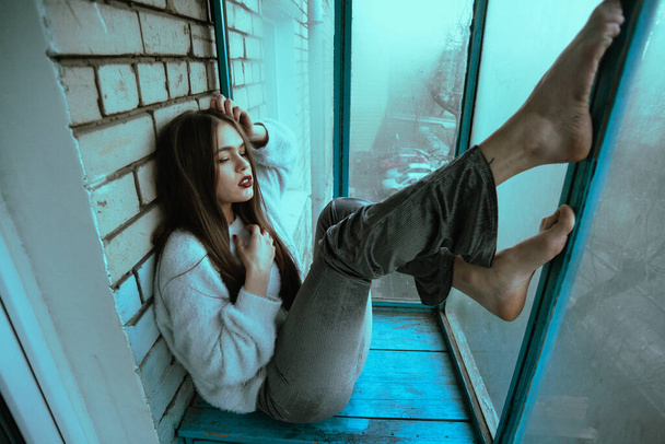 Красива молода сексуальна дівчина позує на балконі. Художній фотопортрет дівчини в сучасному стилі з сидячим і доданим шумом на фото
. - Фото, зображення