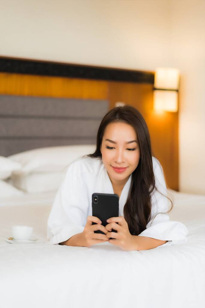 Portré gyönyörű fiatal ázsiai nő használ okos mobiltelefon az ágyban a hálószoba belső - Fotó, kép