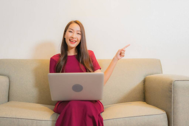Portre güzel genç Asyalı kadın oturma odasındaki koltukta dizüstü bilgisayar kullanıyor. - Fotoğraf, Görsel