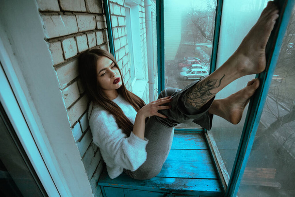 Schöne junge sexy Mädchen posiert auf dem Balkon. Kunst Fotoporträt eines Mädchens in einem modernen Stil mit einer sitzenden und zusätzlichen Lärm auf dem Foto. - Foto, Bild