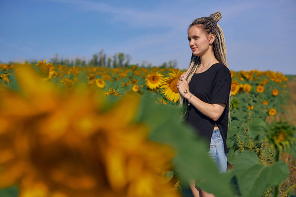 Portrait of a girl who stands in a field with flowering sunflowers - 写真・画像