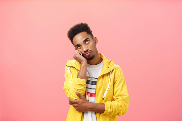 Waist-up shot of bored irritated african american man with beard and afro haircut leaning head on palm in indifferent and careless pose being tired of annoying boring talks over pink background - Photo, Image