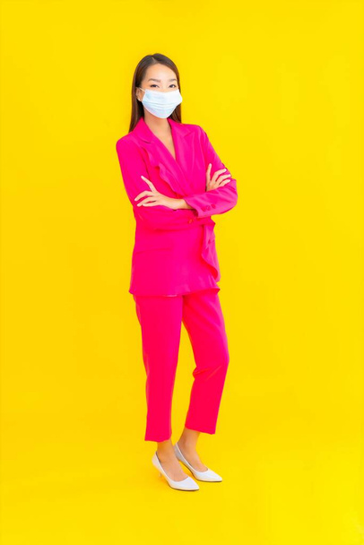 Ritratto bella giovane donna asiatica indossare maschera per proteggere coronavirus o covid19 su sfondo di colore giallo - Foto, immagini