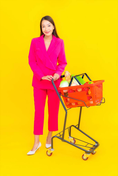 Portrait beautiful young asian woman with basket or cart and grocery from supermarket on color background - Photo, Image