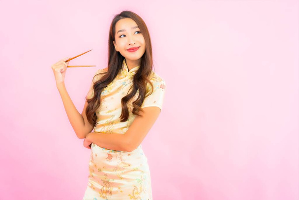 Retrato hermosa joven asiática mujer con palillos sobre fondo rosa - Foto, Imagen
