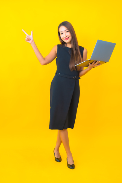 Портрет красивая молодая азиатская деловая женщина с ноутбуком на желтом фоне - Фото, изображение