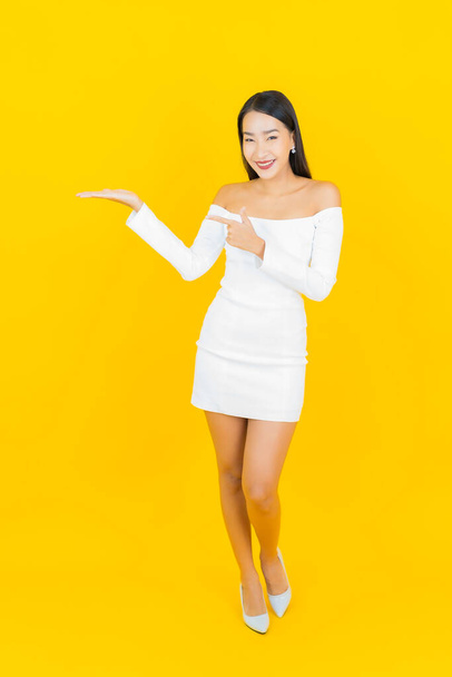 Portré gyönyörű fiatal üzleti ázsiai nő mosollyal és akció sárga háttér - Fotó, kép