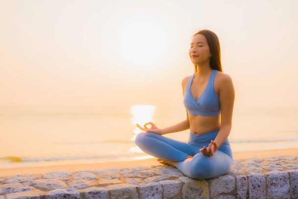 Портрет молодой азиатской женщины делать медитацию вокруг морского берега океана на восходе солнца для здоровья - Фото, изображение