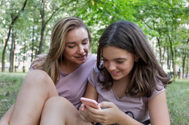 Mamá y su hija adolescente usan un teléfono inteligente para caminar en un parque de verano - Foto, Imagen