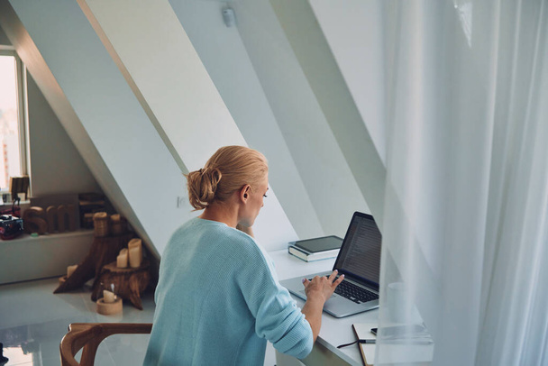 Vista trasera de la mujer joven que usa el ordenador portátil mientras trabaja en casa - Foto, Imagen
