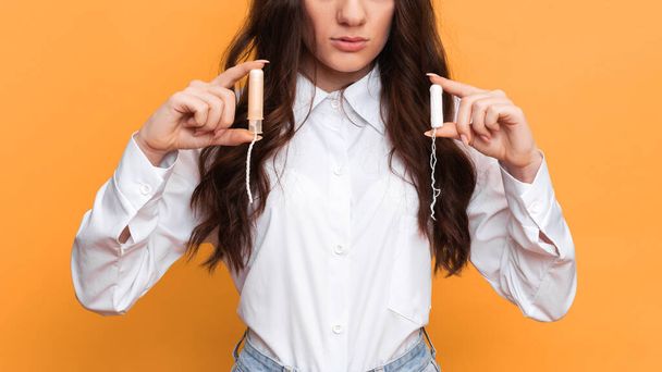 Uma foto de estúdio de uma menina segurando um tampão em um aplicador em uma mão e um tampão sem um aplicador menstrual na outra. - Foto, Imagem