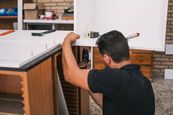Працівник використовує дриль для будівництва кухонних меблів
 - Фото, зображення
