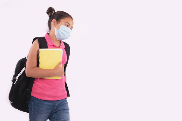 Unhappy little girl student holding notebook and wearing protective mask - Foto, Bild
