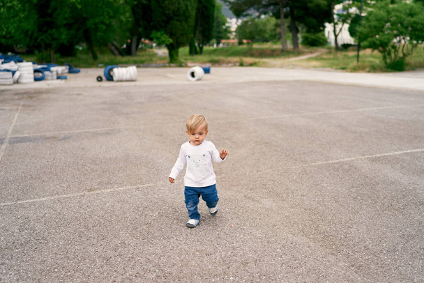 Χαμογελαστό παιδί περπατά σε μια τσιμεντένια παιδική χαρά  - Φωτογραφία, εικόνα