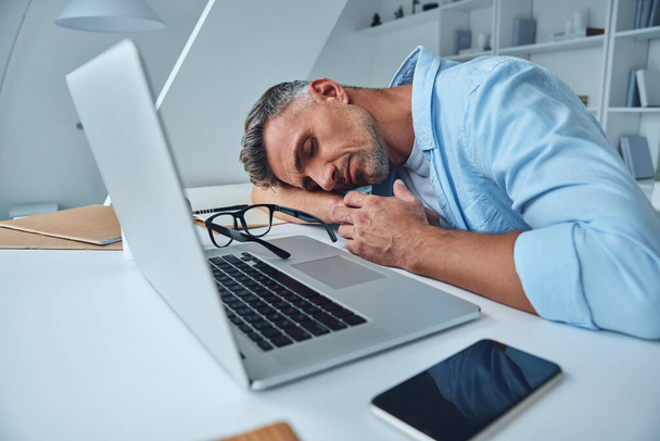 Tired mature man sleeping while sitting at the office desk - Valokuva, kuva