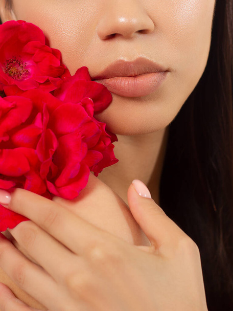 Macro photo of female lips with beautiful skin and nude makeup. light transparent gloss on full lips and red flowers. Fashion photography. Cosmetology and spa. Freshness of spring - Zdjęcie, obraz