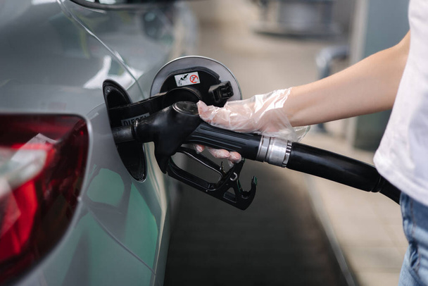 Η γυναίκα ανεφοδιάζεται στο βενζινάδικο. Θηλυκό χέρι πλήρωση βενζίνης καυσίμου βενζίνης στο αυτοκίνητο χρησιμοποιώντας ένα ακροφύσιο καυσίμου. Η έννοια των τιμών του πετρελαίου. Κοντινό πλάνο του χεριού - Φωτογραφία, εικόνα