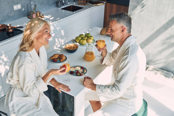 Вид зверху красива зріла пара в халатах насолоджується сніданком разом, проводячи час на домашній кухні
 - Фото, зображення