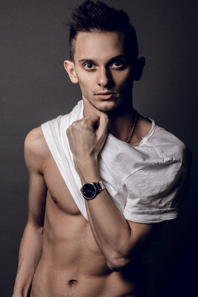 Handsome young man isolated. Portrait in white undershirt muscular man is standing on grey background and looking at camera. You can see the muscles of the abs - Valokuva, kuva