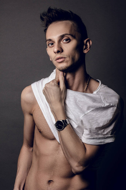 Handsome young man isolated. Portrait in white undershirt muscular man is standing on grey background and looking at camera. You can see the muscles of the abs - Фото, зображення