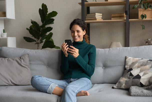 Smiling woman relaxing on couch with smartphone, browsing apps - Φωτογραφία, εικόνα