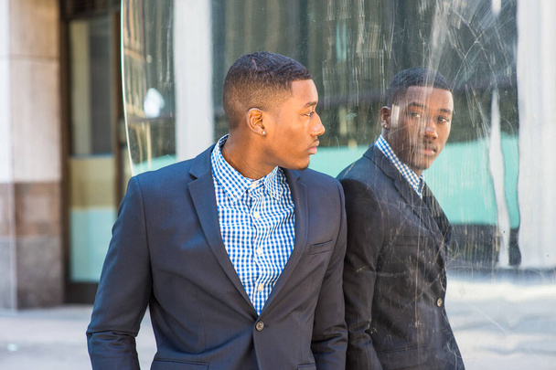 Młody Afroamerykański biznesmen w niebieskiej kurtce, wzorzystej koszuli, stojący przy lustrze, odwracający się, patrzący na odbicie, myślący. Pojęcie pewności siebie, poczucia własnej wartości, samokontroli - Zdjęcie, obraz