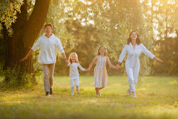 Happy family at sunset. Father, mother and children are running, having fun and enjoying summer evening.  - Photo, image