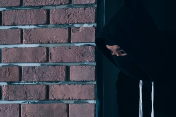 Un ladro vestito di scuro e con un cappotto di pelle rompe una finestra in una residenza. - Foto, immagini