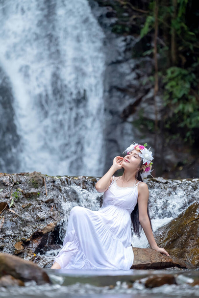 Eine schöne junge Frau entspannt sich in der Natur in der Nähe eines Wasserfalls. - Foto, Bild
