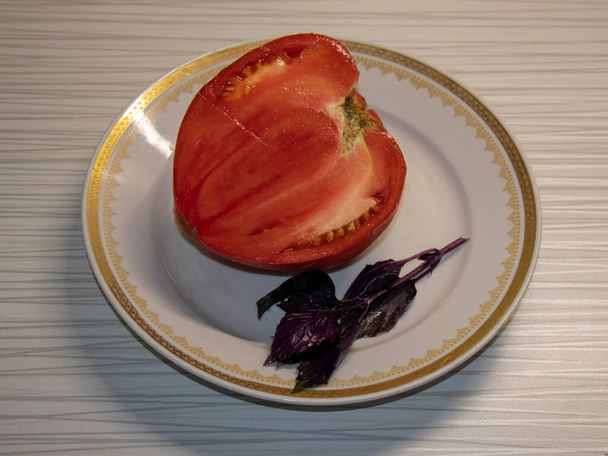 A large red tomato, cut in half, on a plate. - Photo, image