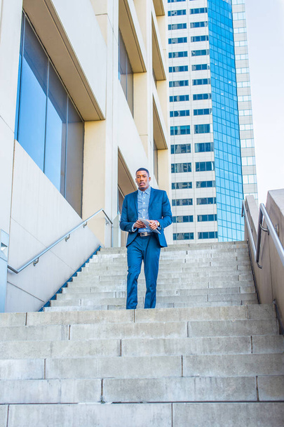 Egy táblagépet tartva, egy fiatal jóképű fekete üzletember magabiztosan sétál le a lépcsőn egy üzleti épület előtt. - Fotó, kép