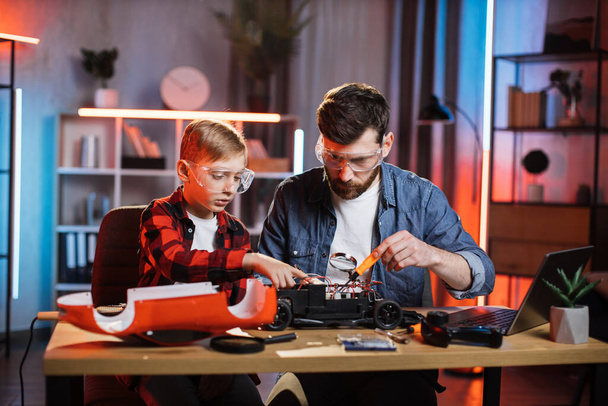 Man and boy using soldering iron for repairing toy car - Foto, Bild