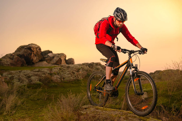 Cyclist in Red Riding Bike on the Spring Rocky Trail at Sunset. Extreme Sport and Enduro Biking Concept. - 写真・画像