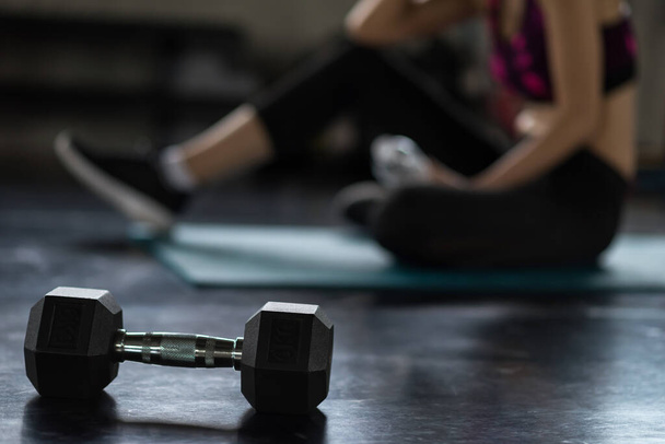 Closeup dumbbell with blur athlete woman break and rest after exercise in fitness sport gym. Weight training, bodybuilding and healthy sport lifestyle concept. - Foto, imagen