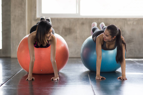 Fit smiling sporty lesbian LGBT couple or friends in plank position exercising on fitness balls in gym. Women working out together for bodybuilding and healthy sport lifestyle. - Fotoğraf, Görsel