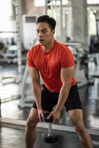Asian muscular strong young man biceps squat exercise by heavy dumbbell in fitness gym. Bodybuilding and healthy lifestyle concept. - Foto, Imagen