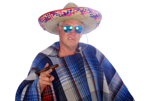 Mężczyzna nosi meksykańskie Sombrero i Serape albo Poncho, okulary przeciwsłoneczne i pali duże cygaro podczas meksykańskich świąt. Izolacja na białym, pokój na tekst. Ścieżka wycinków. Zdjęcie Booth. Mężczyzna ubiera się podczas sesji zdjęciowej na imprezie.  - Zdjęcie, obraz