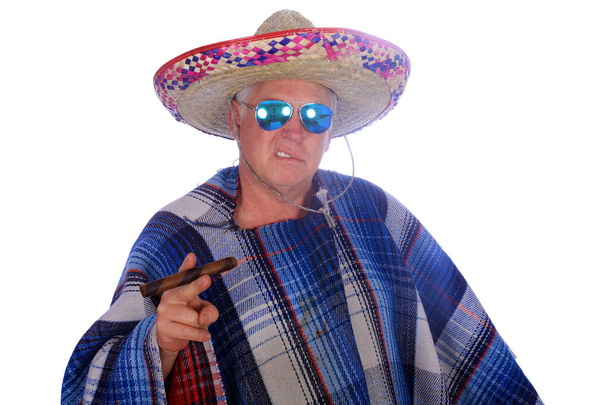 Egy férfi Mexikói Sombrero-t és Serape-et vagy Poncho-t visel, napszemüveget és egy nagy szivart szív, miközben egy mexikói ünnepet ünnepel. Elkülönítve a fehérektől, hely az üzeneteknek. Vágóút. Fotófülke. Egy férfi öltözik, miközben a Photo Booth egy partin.  - Fotó, kép