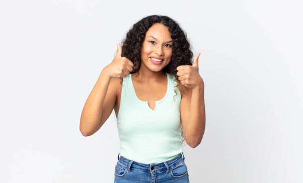 pretty hispanic woman smiling joyfully and looking happy, feeling carefree and positive with both thumbs up - Фото, изображение
