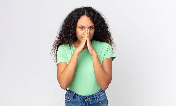 pretty hispanic woman feeling worried, hopeful and religious, praying faithfully with palms pressed, begging forgiveness - Фото, изображение