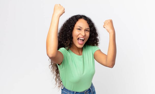 pretty hispanic woman shouting triumphantly, looking like excited, happy and surprised winner, celebrating - Foto, imagen