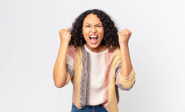 pretty hispanic woman shouting aggressively with an angry expression or with fists clenched celebrating success - 写真・画像