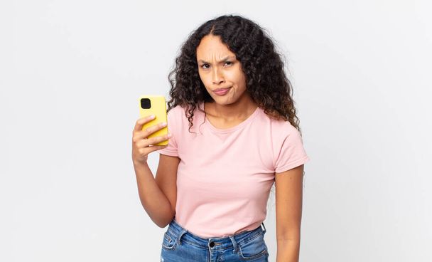 hispanic pretty woman feeling sad, upset or angry and looking to the side and holding a smartphone - Foto, Imagem