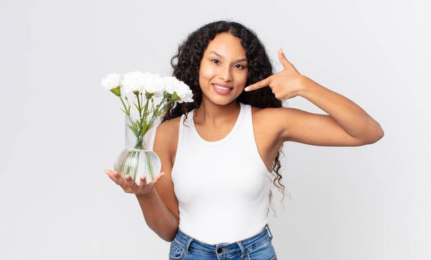 hispanic pretty woman smiling confidently pointing to own broad smile and holding a flowers jar - Φωτογραφία, εικόνα