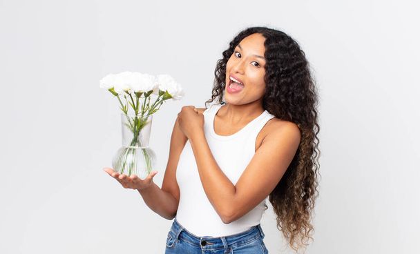 hispanic pretty woman feeling happy and facing a challenge or celebrating and holding a flowers jar - Foto, immagini