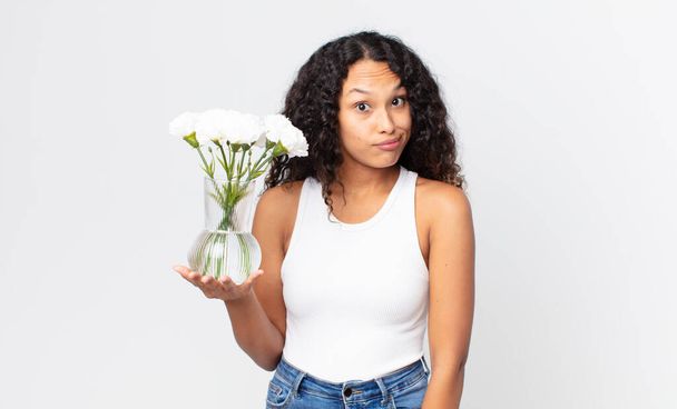 hispanic pretty woman feeling puzzled and confused and holding a flowers jar - Фото, зображення