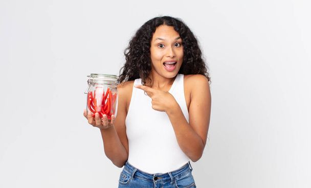 hispanic pretty woman looking excited and surprised pointing to the side and holding  red liquorice jelly bean - Fotó, kép